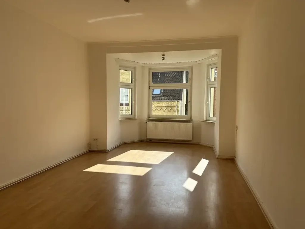 Nachher: dasselbe Wohnzimmer mit Erkerfenster, leer geräumt, Sonnenlicht fällt auf den sauberen Boden